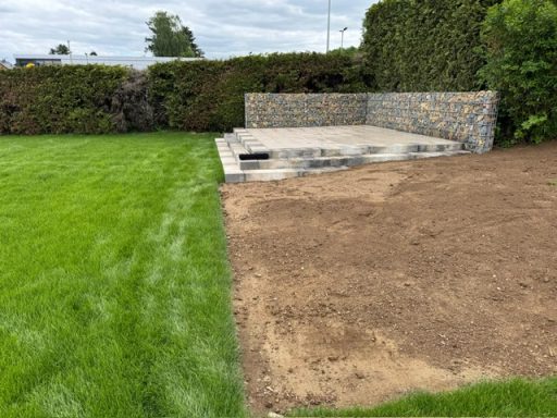 Gabionen, Terrasse Rasenfläche neben einem gepflasterten Bereich und einer Steinmauer.