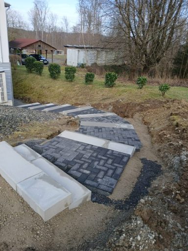 Treppenaufgang Gepflasterter Weg mit grauen Steinen zwischen Rasen und Büschen in einer Gartenlandschaft.